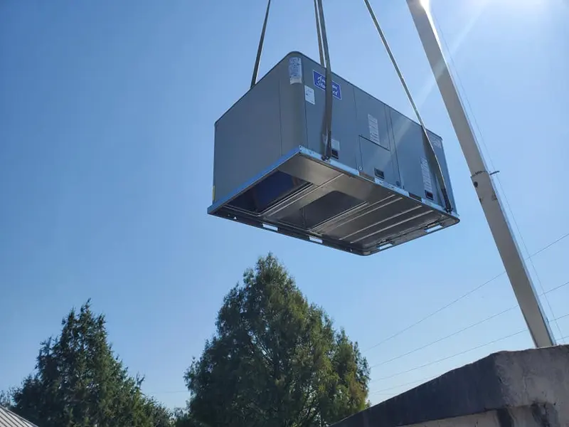 A packaged rooftop unit being lifted into place by crane