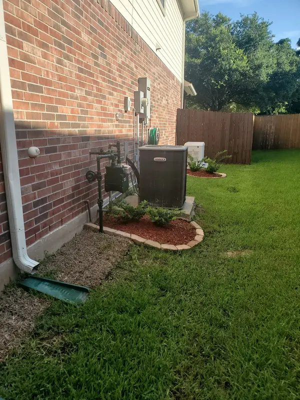 Outdoor AC unit installed in a landscaped bed beside a home