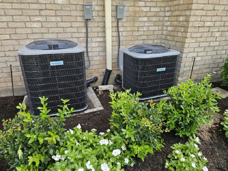 Two outdoor AC units installed in a landscaped flower bed
